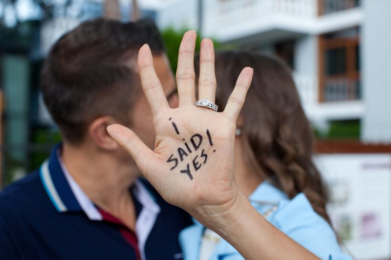 Man and woman kissing behind her hand with the words I said yes